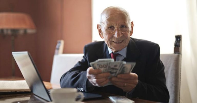Smart Investments - Confident senior businessman holding money in hands while sitting at table near laptop